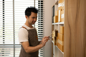 A man is standing in front of a shelf full of boxes and looking at a tablet. He is holding a box in his hand

