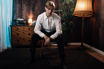 Handsome Guy in a Retro Old Scene Sits on an Old Ladder and Looks at the Camera, Exuding Timeless...