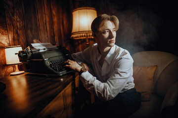 Young Vintage Blonde Man Sits at a Retro Typewriter Machine Writing a Letter, Gazing and looking to...