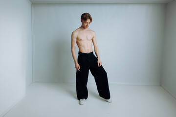 shirtless high fashion male model stand in white box studio and pose while look down