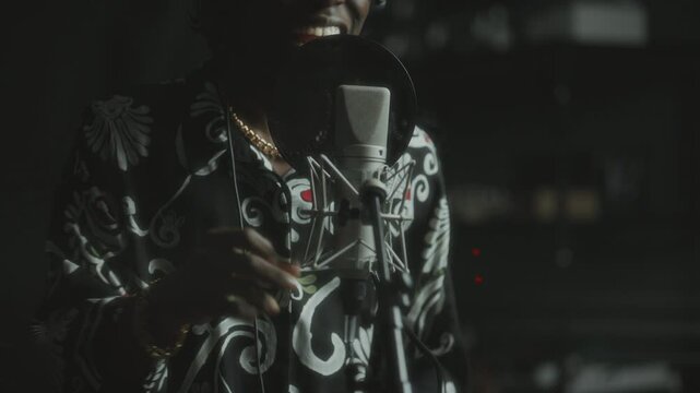 African American male performer in headphones and stylish sunglasses, singing emotionally into microphone in professional recording studio