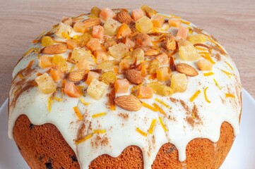 An appetizing fruitcake with creamy icing, almonds, and candied fruit sits on a plate, inviting a...