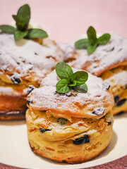 Several delightful currant buns sit elegantly on a plate, adorned with powdered sugar and fresh mint.
