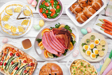 Traditional Easter ham dinner. Top down view table scene on a white wood background. Ham, scalloped potatoes, vegetable side dishes, eggs, breads and lemon cake dessert.