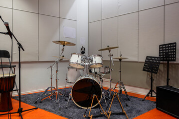 White drum set with cymbals in a music rehearsal room with acoustic panels, microphone, and music stands, creating a professional practice space