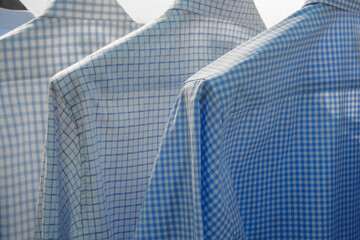 Three blue and white plaid shirts hanging on a rack. The shirts are all different shades of blue...