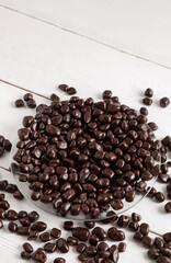 Dried fruits and berries in brown chocolate glaze. Candies on a white wooden background.