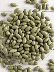 Chocolate-glazed nuts. Green candies on a white wooden background.