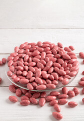 Chocolate-covered nuts on a white wooden background. Pink candies in a clear glass plate.