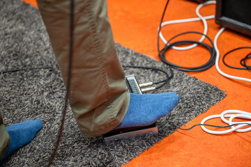 Foot of guitarist pressing pedal of electric guitar with cables in music studio