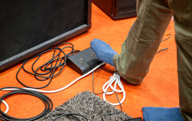 Foot of guitarist pressing pedal of electric guitar with cables in music studio