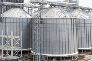 cylindrical metal grain silos with conical roofs are aligned in a row © debjit