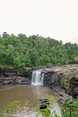 Obraz premium Scenic waterfall cascading into a rocky pool surrounded by lush forest