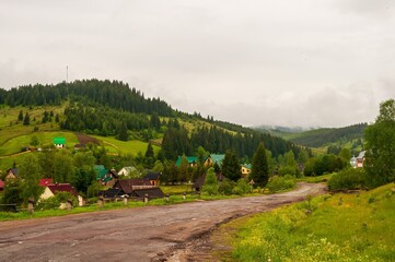 Naklejka premium A picturesque village nestled in a green valley under a cloudy sky offers a scenic mountain view.