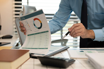 A man is pointing at a piece of paper on a desk. The paper has a business-related title and the man...