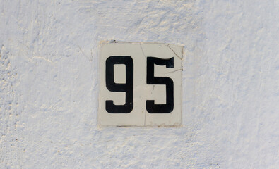Street address number, number 95. Black numbers on a white stucco wall.