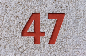 Red street address number, number 47, impressed into a rough white stucco wall.