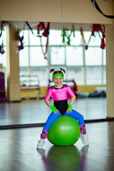 Naklejka premium A small, beautiful girl, in athletic form, trains in the gym with a fitball