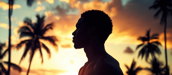Man stands in silhouette against a vibrant sunset backdrop with palm trees on a tropical beach
