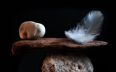 A symbolic balance between a delicate feather and a heavy stone placed on a piece of driftwood, representing contrast, justice, equality, or philosophical concept