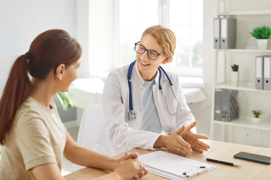 Young female doctor physician or cardiologist in white coat with stethoscope around her neck smiling while talking to woman patient in medical office. Professional consultation and friendly atmosphere