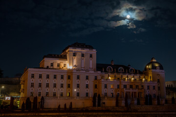 A nighttime view of Macedonia Square, the central plaza of Skopje. Illuminated buildings, monuments, and fountains create a vibrant atmosphere in the heart of the city.