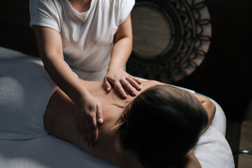 Close-up of professional female masseuse giving relaxing back massage to young unrecognizable woman...