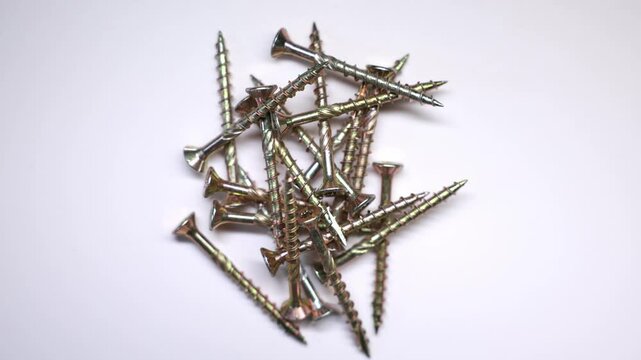 A scattered pile of golden metallic screws with threaded bodies and flat countersunk heads, displayed against a plain white background.