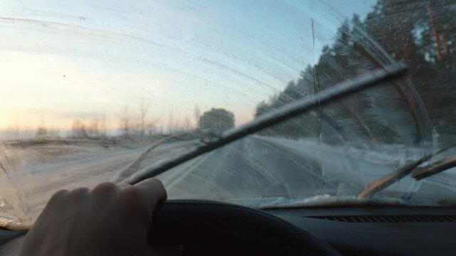 Windshield Wipers Clean Car Windshield From Frozen Precipitation During Challenging Winter Drive, Navigate Icy Road In Golden Sunset With Limited Visibility. Windshield washer fluid is frozen.