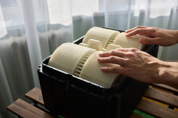 Hands are carefully handling industrial filters while inside a well-organized storage box