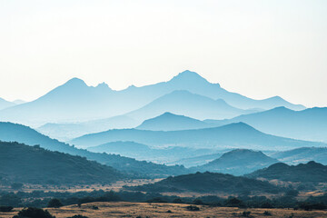 Obraz premium Layered mountain landscape with misty blue hues and rolling hills under a clear sky.