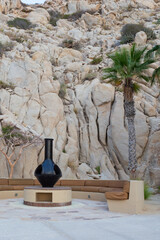 Black chimenea surrounded by a stone mountain and seating at the seaside resort with palm trees.