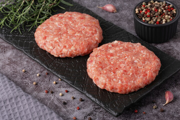 Fresh ground meat patty ready for cooking with herbs and garlic on a dark plate