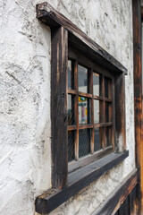 Small Japanese business with weathered wooden-framed window set into a rough, off-white stucco...