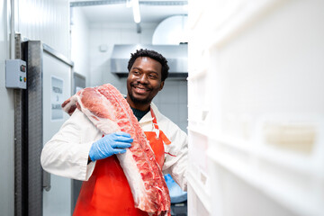 Slaughterhouse worker holding pork meat in cold storage butchery shop.