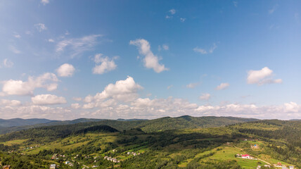 Fototapeta premium Majestic Mountains, Lush Green Forests, And Soft White Clouds On A Sunny Day. Aerial View Showcasing The Stunning Beauty Of Nature From A High Perspective. 