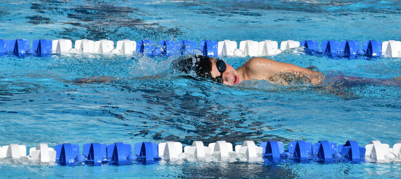 A young boy at swim practice in an outdoor pool practicing his strokes.