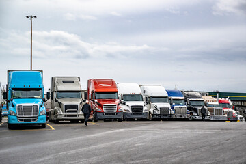 Truck drivers walk to their big rig semi trucks with loaded semi trailers standing in row on truck stop parking lot for the rest © vit