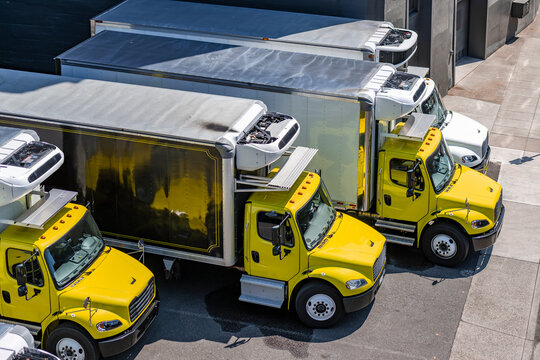 Yellow and white middle duty day cab rigs semi trucks with refrigerated box trailers standing in row on the industrial parking lot waiting for the next local deliveries