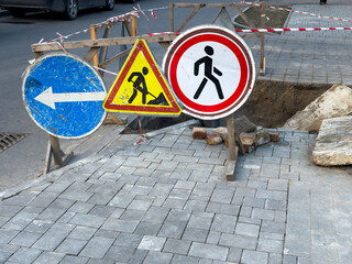Construction signs are placed near a sidewalk that is undergoing repairs, indicating a pedestrian...