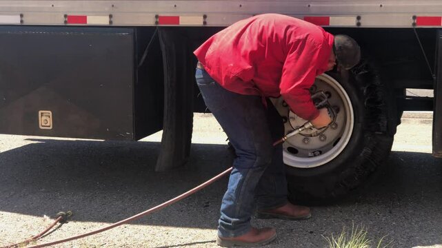 Man Usuing Pneumatic Impact Wrench To Change a Truck Tire on side of Highway