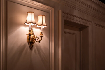 Elegant vintage wall sconce with dual fabric lampshades casts a warm, atmospheric glow on a classic...