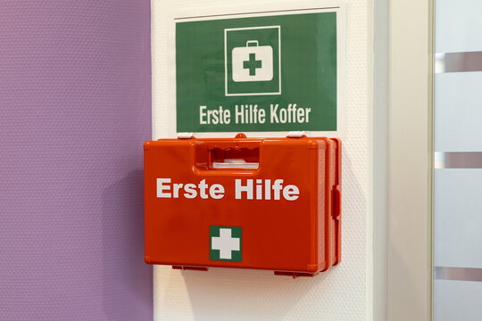 Red first aid kit mounted on a wall with clear health and safety signage in a well-lit environment