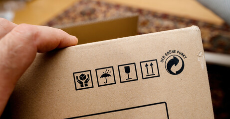 A person holds a Hi-Fi equipment package made of cardboard, featuring handling symbols for fragile,...