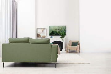 Stylish living room with cozy sage color sofa, TV set and fireplace. Interior design