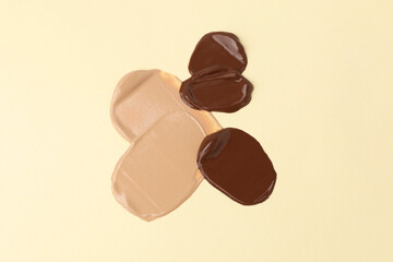 Samples of different foundations on beige background, above view