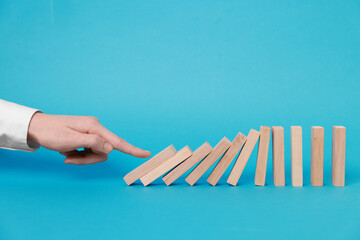 Domino effect. Woman pushing wooden blocks on light blue background, closeup