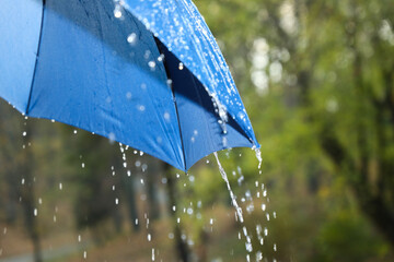 Open blue umbrella under pouring rain outdoors, closeup