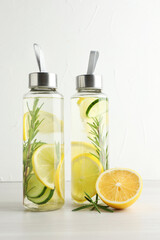 Lemon water with slices of cucumber in bottles, rosemary and fresh fruit on beige table