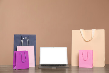 Internet shopping. Laptop and colorful paper bags on wooden table against brown background